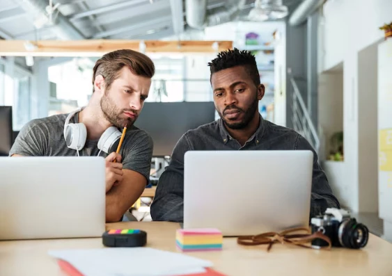 Deux collègues consultant des ordinateurs portables avec un appareil photo sur la table.